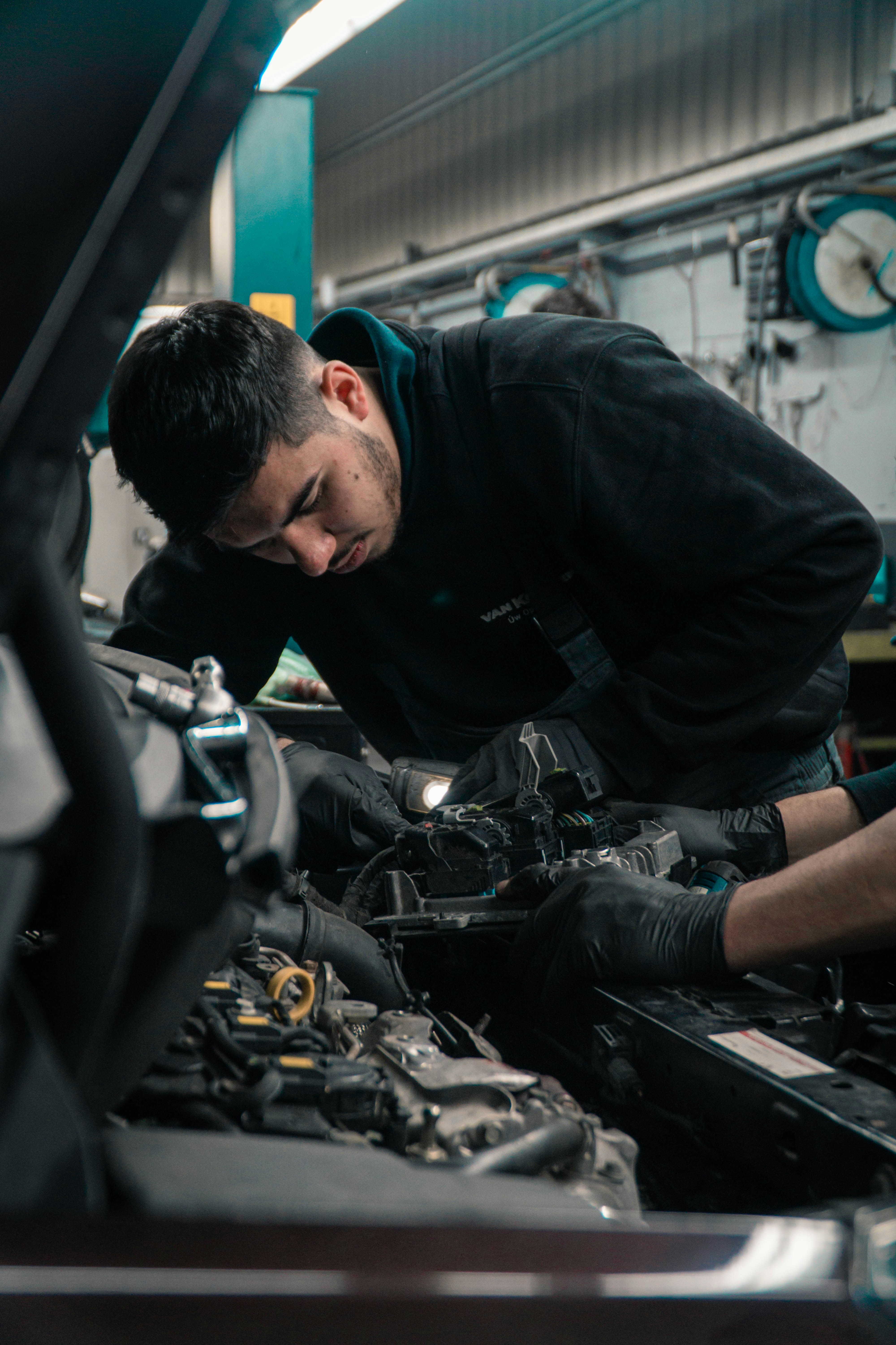Mechaniker arbeitet konzentriert mit einer Lampe im Motorraum eines Fahrzeugs